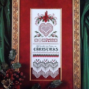 May include: Framed Christmas cross-stitch with a red and gold ornate frame. The design features a heart, holly, and the text "All hearts are home on CHRISTMAS." The bottom has a white lace-like border.