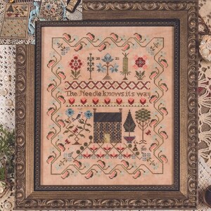May include: A framed cross-stitch sampler with a pink background and a brown house in the center. The sampler is titled "Needle be True Sampler & Smalls" and includes the text "The Needle knows its way".
