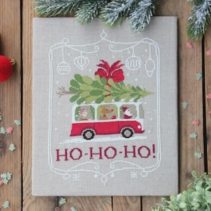 Op de afbeelding: Kruissteekontwerp met een rode bus die een kerstboom vervoert, met de tekst "HO-HO-HO!". De bus heeft passagiers, waaronder een rendier en de kerstman. Het ontwerp staat op een neutrale stof, met feestelijke decoraties.