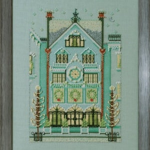 May include: A cross-stitch pattern of a blue house with white trim and a clock on the front. The house is decorated with wreaths and lights. There are two trees on either side of the house.