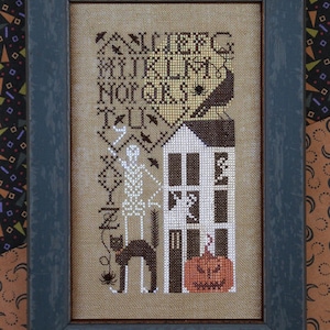 May include: A framed cross-stitch design featuring a spooky house with a jack-o'-lantern, a black cat, a skeleton, and bats. The design includes the text "Trick or Treat" and "Happy Halloween".