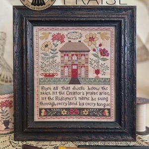 May include: A framed cross-stitch sampler featuring a house, flowers, birds, and the year 2024. The text reads: From all that dwells below the skies, let the Creator's praise arise; let the Redeemer's name be sung through every land by every tongue.