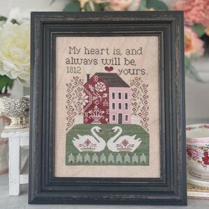 Peut inclure: Image d'une broderie encadrée avec une maison et des cygnes. Le texte dit : « Mon cœur est, et sera toujours, à vous ». L'œuvre est dans un cadre noir. La maison est rouge et rose, et les cygnes sont blancs.