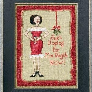 May include: Cross-stitch artwork in a black frame. The image features a woman in a red dress holding a cocktail, with the text "Just Hoping for Mr. Right NOW!" and a sprig of mistletoe. The artwork has a red beaded border.