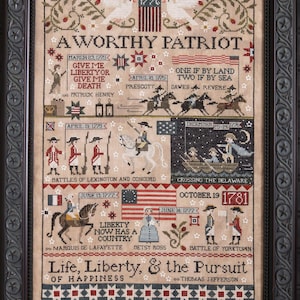 May include: A framed cross-stitch sampler with a patriotic theme. The design features historical figures, dates, and phrases like "Give Me Liberty or Give Me Death." The color palette includes red, white, and blue, with a black frame.