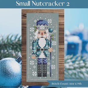 May include: A cross-stitch pattern depicting a nutcracker soldier in a blue and white uniform, with a white beard and a blue hat. The text "Small Nutcracker 2" is at the top. The stitch count is 36w x 79h.