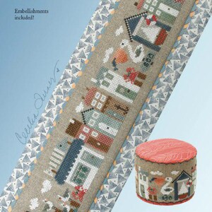 May include: A cross-stitch pattern titled Seaside Tiny Town by Heart in Hand Needleart, featuring a vertical linen strip with stitched coastal houses, a lighthouse, and a pelican, alongside a small round pincushion with matching motifs.