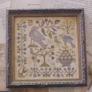 May include: Framed cross-stitch artwork featuring two blue birds perched on branches and a birdhouse. The design includes floral elements and a decorative border, all in shades of blue, green, and brown. The artwork is displayed in a dark wooden frame.