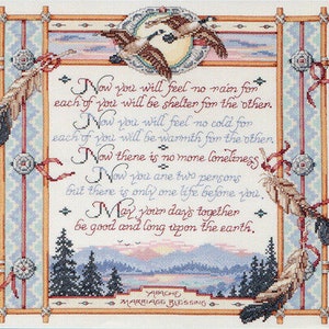May include: Cross-stitch artwork featuring an Apache marriage blessing. The design includes a central text with a decorative border, feathers, and a landscape scene with mountains and trees. The color palette includes beige, blue, and red.
