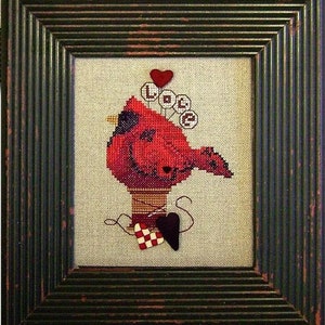 May include: Cross-stitch artwork featuring a red cardinal bird on a thread spool, with the word "LOVE" and a heart above. Includes a black heart and a checkered heart. The framed piece has a dark green, distressed wooden frame.