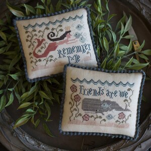 Peut inclure: Deux housses de coussin brodées sur le thème nautique. Le premier coussin représente une sirène avec le texte "Remember Me". Le deuxième coussin représente une baleine avec le texte "Friends Are We".
