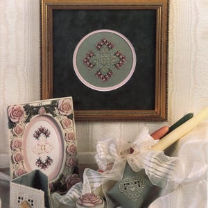 May include: An assortment of handcrafted items, including framed cross-stitch art, a decorative box, and a small pouch. The framed art features a circular design with floral patterns. The color palette includes shades of green, pink, and cream.