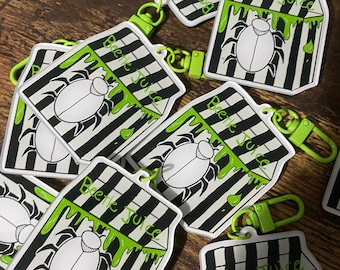 May include: A set of six black and white striped keychains with a green dripping liquid and a cartoon beetle. Each keychain has the text "Beetle Juice" printed on it.