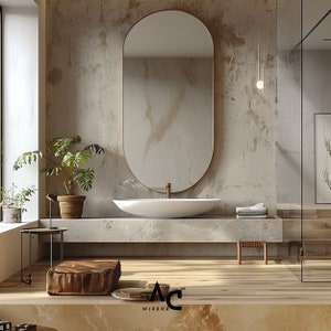 May include: A modern bathroom with a white oval sink, a large oval mirror with a gold frame, and a concrete countertop. The bathroom has a light brown wood floor and a concrete wall with a textured finish.