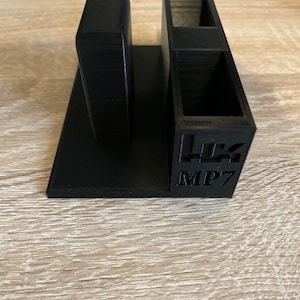 May include: Black 3D printed organiser with two compartments and a single slot. The organiser has the text "MP7" printed on the front.