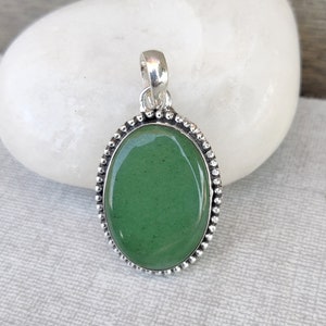 May include: A silver pendant with a green oval gemstone set in a beaded border.