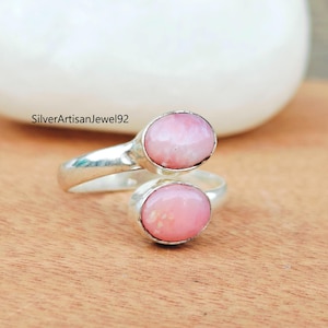 Puede incluir: Un anillo de plata con dos piedras ovaladas de color rosa. El anillo está diseñado para llevarse en la articulación del dedo.
