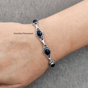 May include: A silver bracelet with four black oval gemstones. The bracelet has a delicate chain design.