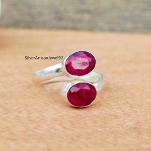 May include: A silver ring featuring two oval-shaped ruby gemstones. The ring is designed to wrap around the finger.