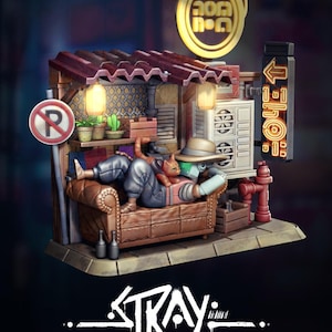May include: A detailed miniature diorama featuring a figure reclining on a brown leather couch, with a cat. The scene includes a shop facade, a no parking sign, and the word "STRAY" in stylized lettering. The diorama has a warm, inviting colour palette.