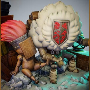 May include: A whimsical, detailed sculpture featuring two wooden figures. One is a brush with a pink bristle, the other a doll-like figure. A large, fluffy, white figure with a shield is also present. The figures are set on a rocky base with a treasure chest.