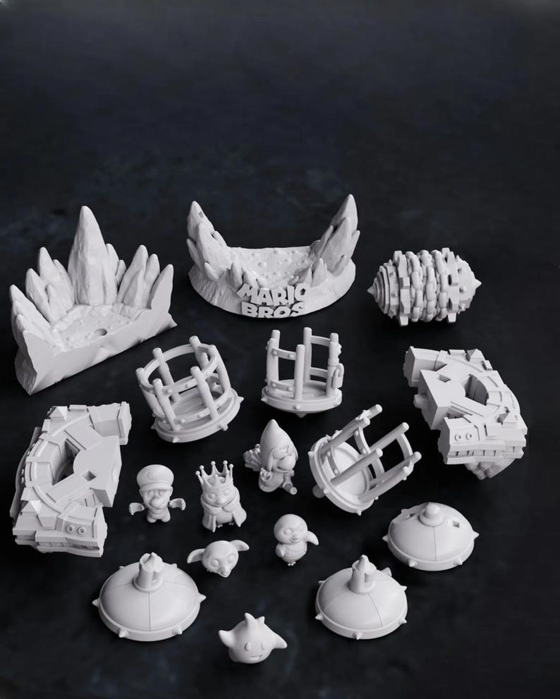 May include: A collection of white 3D-printed figurines and set pieces, including characters, platforms, and architectural elements. The text "MARIO BROS" is visible on one of the set pieces. The figurines include a character wearing a crown.