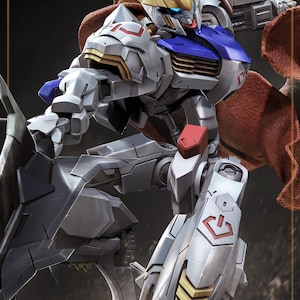 May include: A detailed robot action figure featuring a white, blue, and grey armoured body with gold head accents and a red fabric cape. The figure is posed dynamically, holding a large dark grey weapon, with red markings on the shoulder and leg armour.