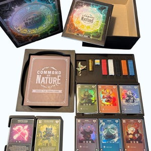May include: A board game set, "Command of Nature," featuring a black box with a colorful circular design. Inside are rule books, cards, and game pieces. The cards display character illustrations and game information. The set includes various colored tokens.