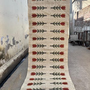 May include: A beige area rug with a repeating pattern of red and green stylized flowers. The rug has fringe on the bottom edge.