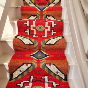 Puede incluir: Un corredor de alfombra rojo, naranja y blanco con dise&ntilde;os geom&eacute;tricos. El corredor se coloca en un conjunto de escaleras blancas.