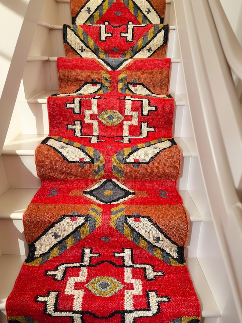 Puede incluir: Un corredor de alfombra rojo, naranja y blanco con dise&ntilde;os geom&eacute;tricos. El corredor se coloca en un conjunto de escaleras blancas.
