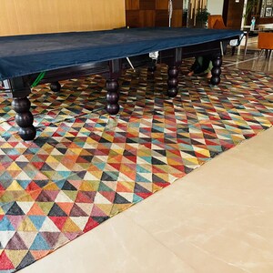 May include: A dark blue pool table cover with a wooden frame and legs. The table is set up on a colorful geometric patterned rug.