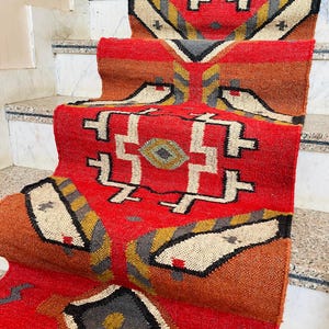 Puede incluir: Un tapete de corredor rojo, naranja y gris con dise&ntilde;os geom&eacute;tricos. El tapete est&aacute; doblado y colocado en un conjunto de escaleras.
