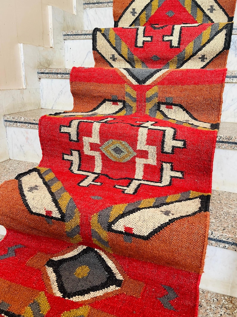 Puede incluir: Un tapete de corredor rojo, naranja y gris con dise&ntilde;os geom&eacute;tricos. El tapete est&aacute; doblado y colocado en un conjunto de escaleras.