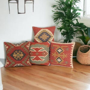 Könnte beinhalten: Vier dekorative Kissen mit einem geometrischen Muster in Rot-, Grün-, Blau- und Beigetönen. Die Kissen liegen auf einem Holzboden.