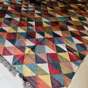 May include: A colorful rug with a geometric pattern of triangles in shades of red, blue, green, yellow, and brown. The rug has a fringe border.