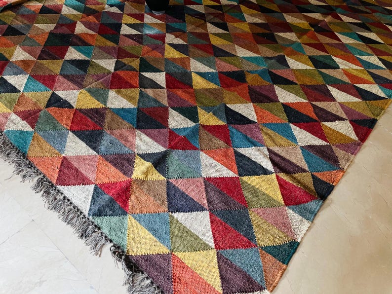 May include: A colorful rug with a geometric pattern of triangles in shades of red, blue, green, yellow, and brown. The rug has a fringe border.