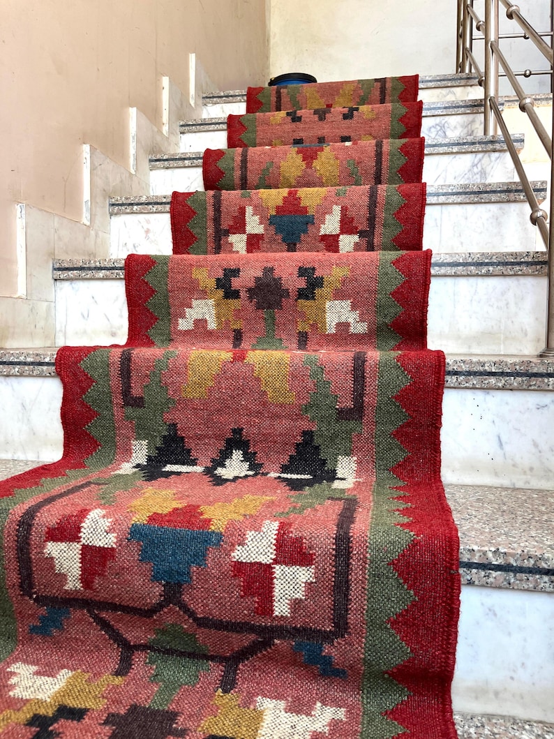 May include: A stair runner with a geometric pattern in shades of red, pink, green, yellow, and black. The runner is installed on marble stairs with a metal handrail.