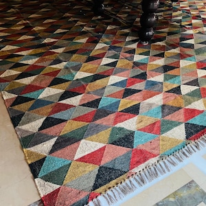 May include: A colorful geometric patterned rug with a fringe border. The rug is made of woven jute and features a variety of colors, including red, blue, green, and brown.