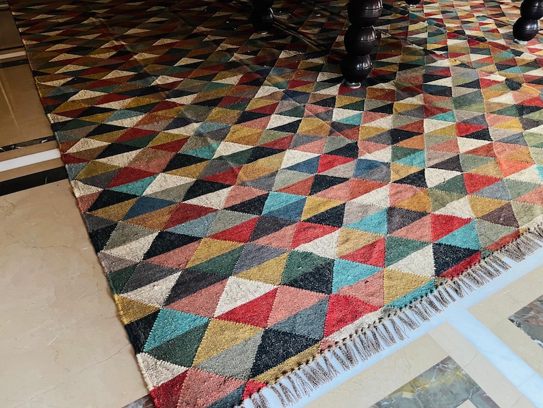 May include: A colorful geometric patterned rug with a fringe border. The rug is made of woven jute and features a variety of colors, including red, blue, green, and brown.