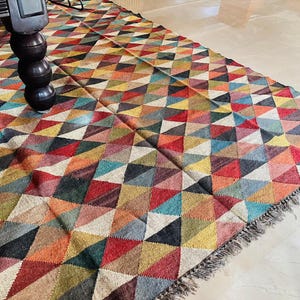 May include: A colorful rug with a geometric pattern of triangles in shades of red, blue, green, yellow, and brown. The rug has a fringe border.