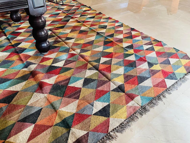 May include: A colorful rug with a geometric pattern of triangles in shades of red, blue, green, yellow, and brown. The rug has a fringe border.