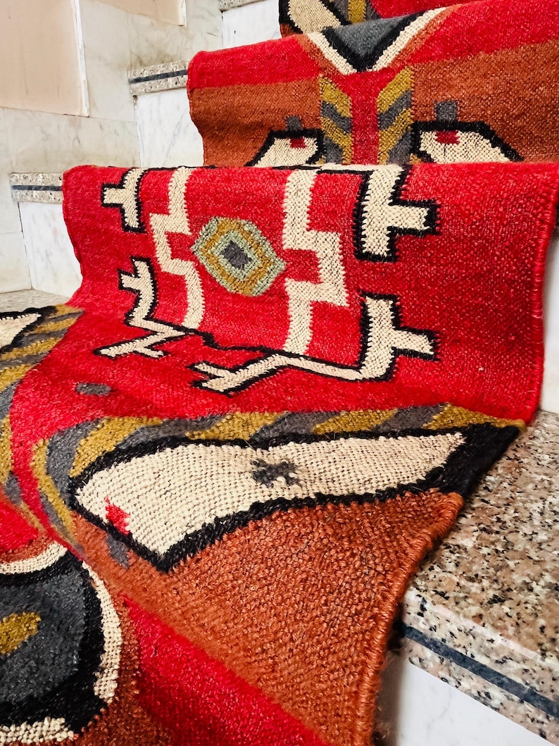 Puede incluir: Una alfombra roja, marr&oacute;n y blanca con dise&ntilde;os geom&eacute;tricos. La alfombra est&aacute; hecha de tejido tejido y tiene un borde con flecos.