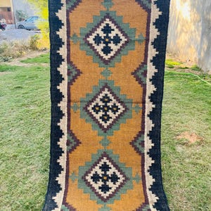 May include: A long, rectangular rug with a black, brown, and green geometric pattern. The rug has a fringe on the bottom edge.