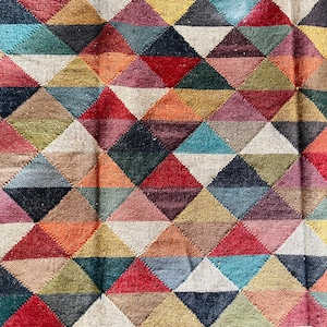 May include: A colorful rug with a geometric pattern of triangles in various shades of red, blue, green, yellow, and brown. The rug has a woven texture and a fringe border.