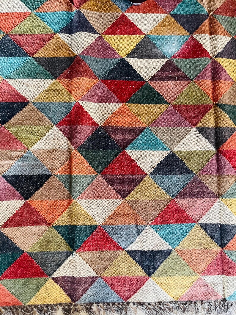 May include: A colorful rug with a geometric pattern of triangles in various shades of red, blue, green, yellow, and brown. The rug has a woven texture and a fringe border.