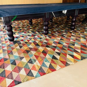 May include: A dark blue pool table cover with a patterned rug underneath. The table has six legs and is made of dark wood.