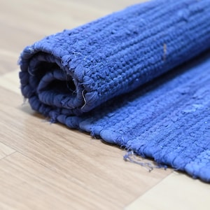 Puede incluir: Una alfombra azul enrollada. La alfombra está hecha de tela tejida, con textura visible y un borde ligeramente deshilachado. El color es un azul profundo y saturado, y la alfombra está parcialmente enrollada, revelando su construcción en capas.
