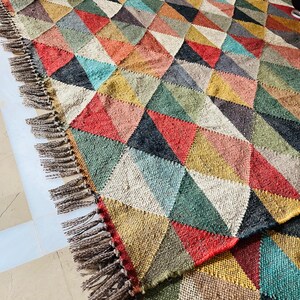May include: A colorful geometric rug with a fringe border. The rug is made of woven fabric and features a pattern of triangles in shades of red, green, blue, yellow, and brown.