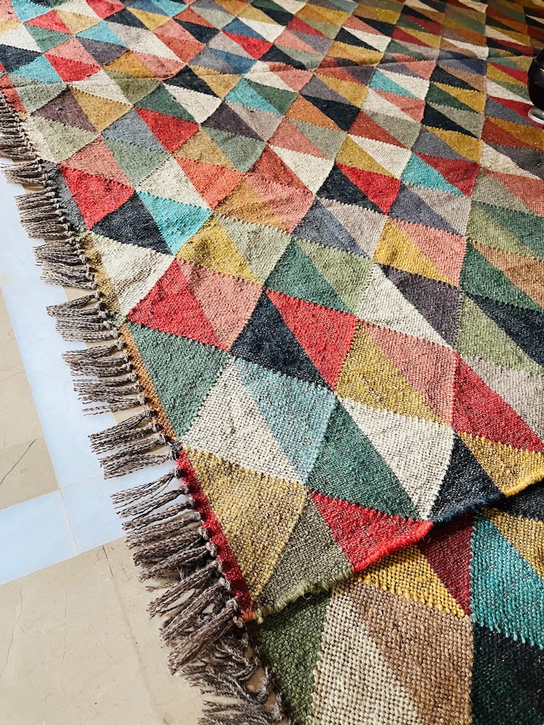 May include: A colorful geometric rug with a fringe border. The rug is made of woven fabric and features a pattern of triangles in shades of red, green, blue, yellow, and brown.